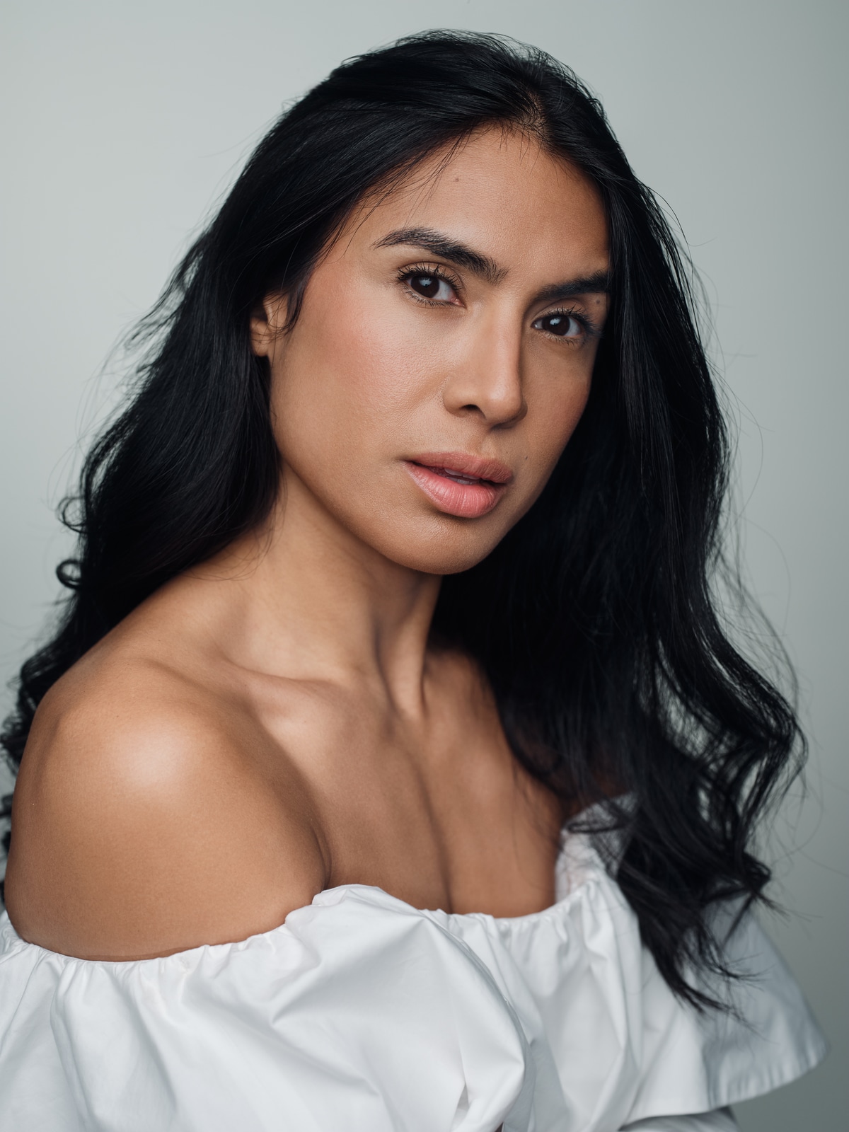 Yasmine Seifi looking towards the camera over her shoulder, with loose hair and a white blouse.